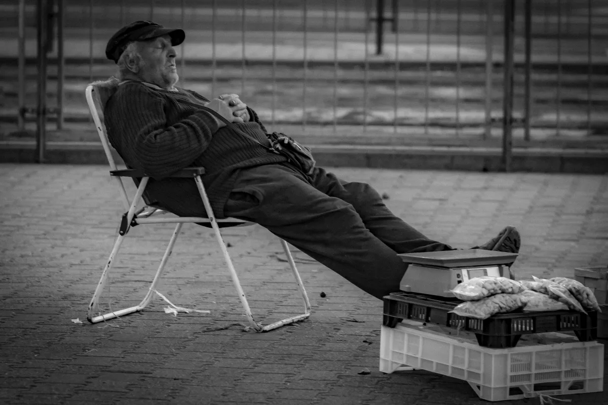 Older market seller reclining on a folding chair beside crates of produce
